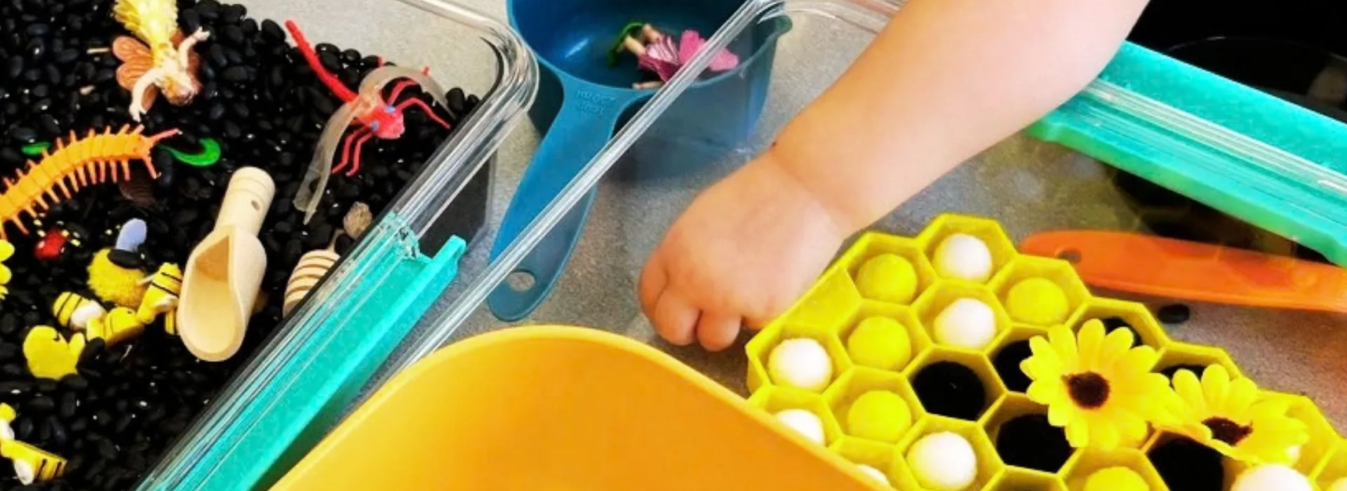 toddler hand reaching into bumble bee sensory bin filled with beans